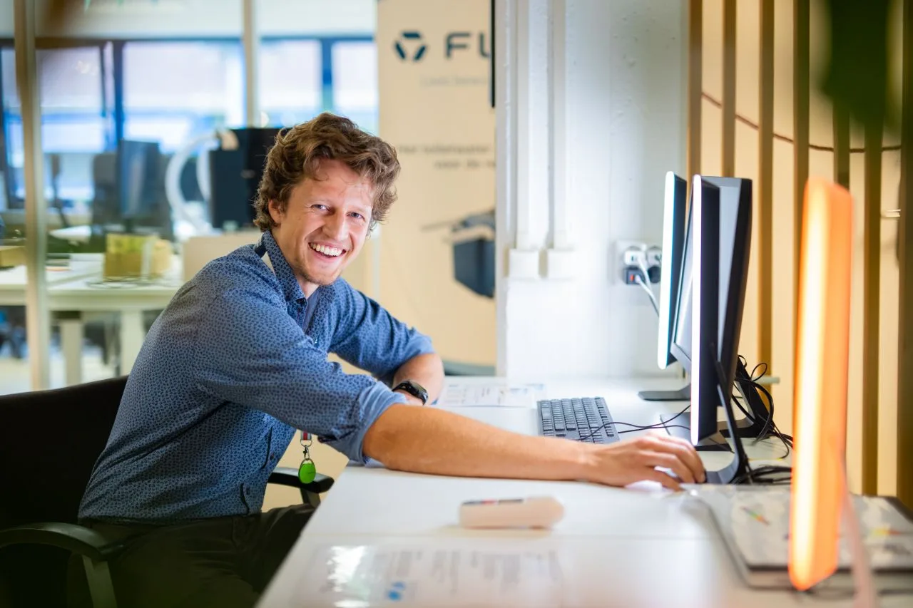 Florian van OPAL lachend aan een bureau met een brandende OPAL Energy Bar naast zijn scherm